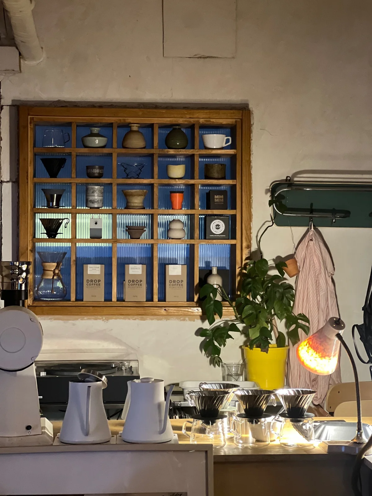 Pour-over brewers and white kettles beneath a wooden display of cups and coffee tools at Always August in Mangwon.