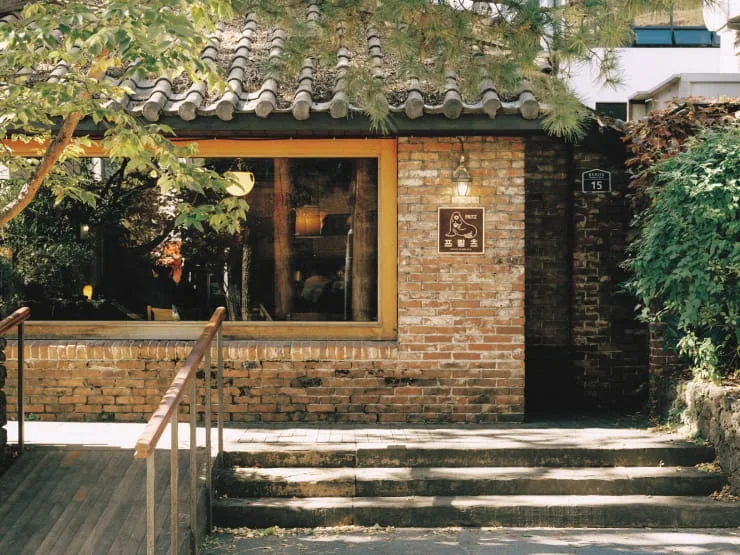 Brick house and tiled roof with a Fritz sign and pine tree within the Jangchung café complex.